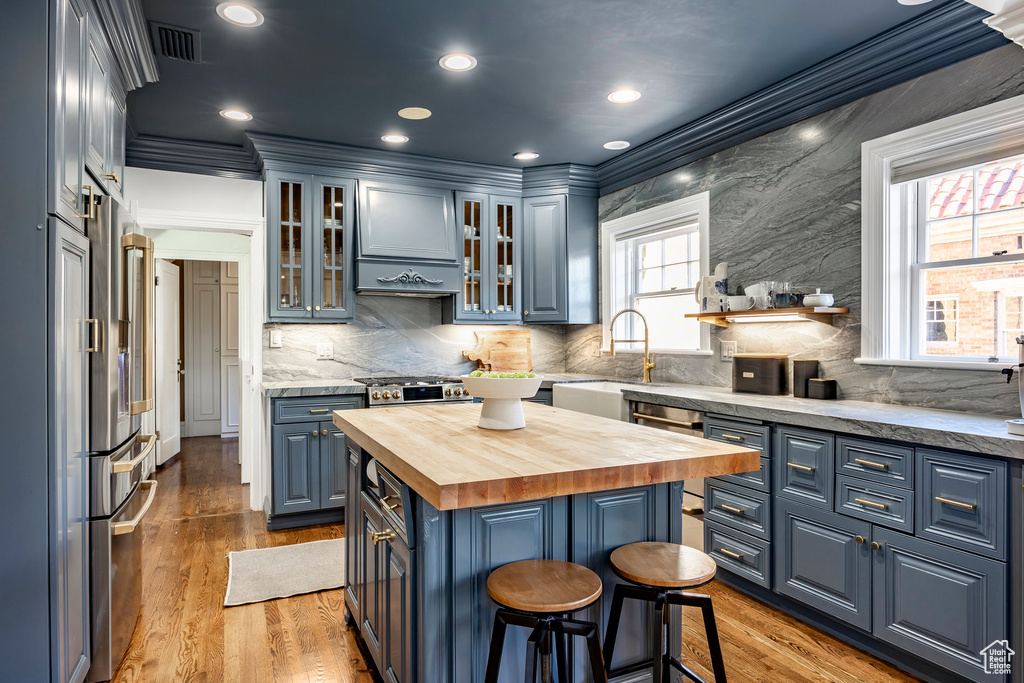 Kitchen with a center island, blue cabinetry, a kitchen breakfast bar, butcher block countertops, and ornamental molding