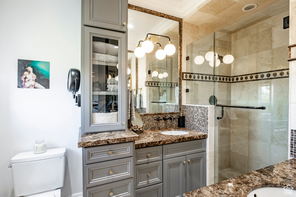 Bathroom with ornamental molding, vanity, an enclosed shower, toilet, and decorative backsplash