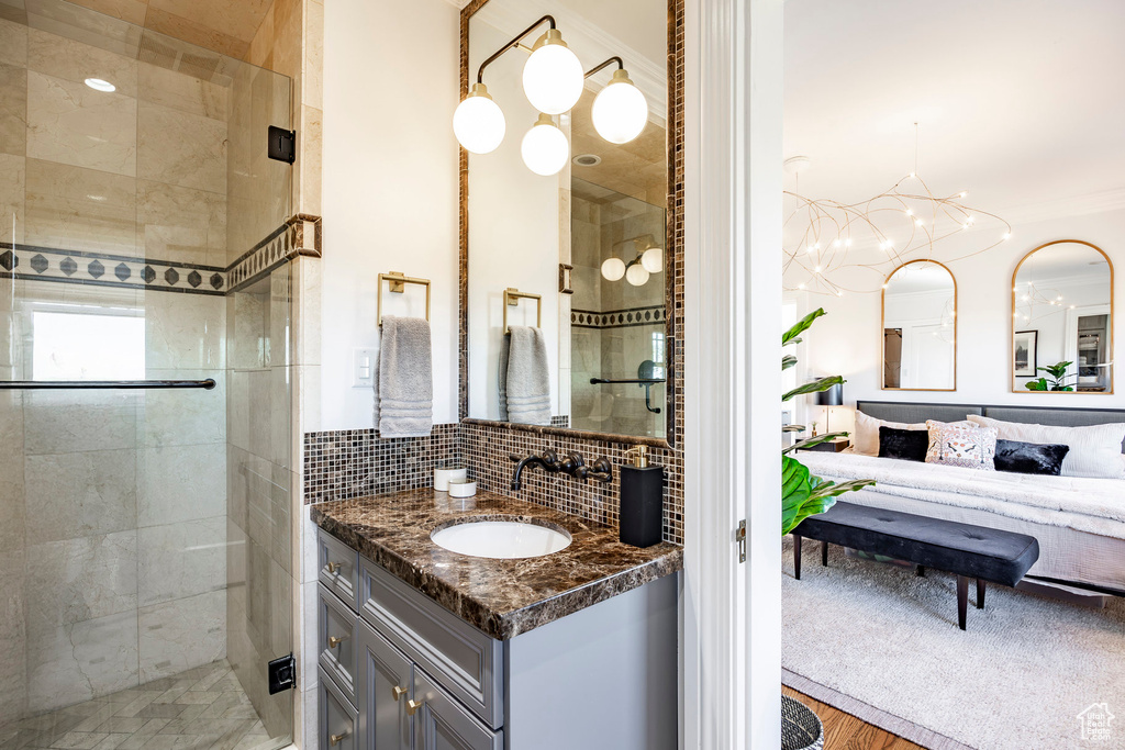 Bathroom featuring tasteful backsplash, wood-type flooring, vanity, a notable chandelier, and a shower with shower door