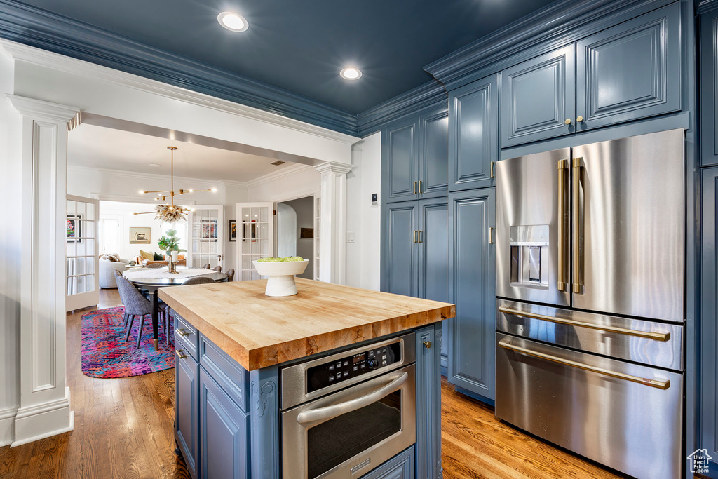 Kitchen featuring blue cabinetry, light wood-type flooring, appliances with stainless steel finishes, and decorative light fixtures