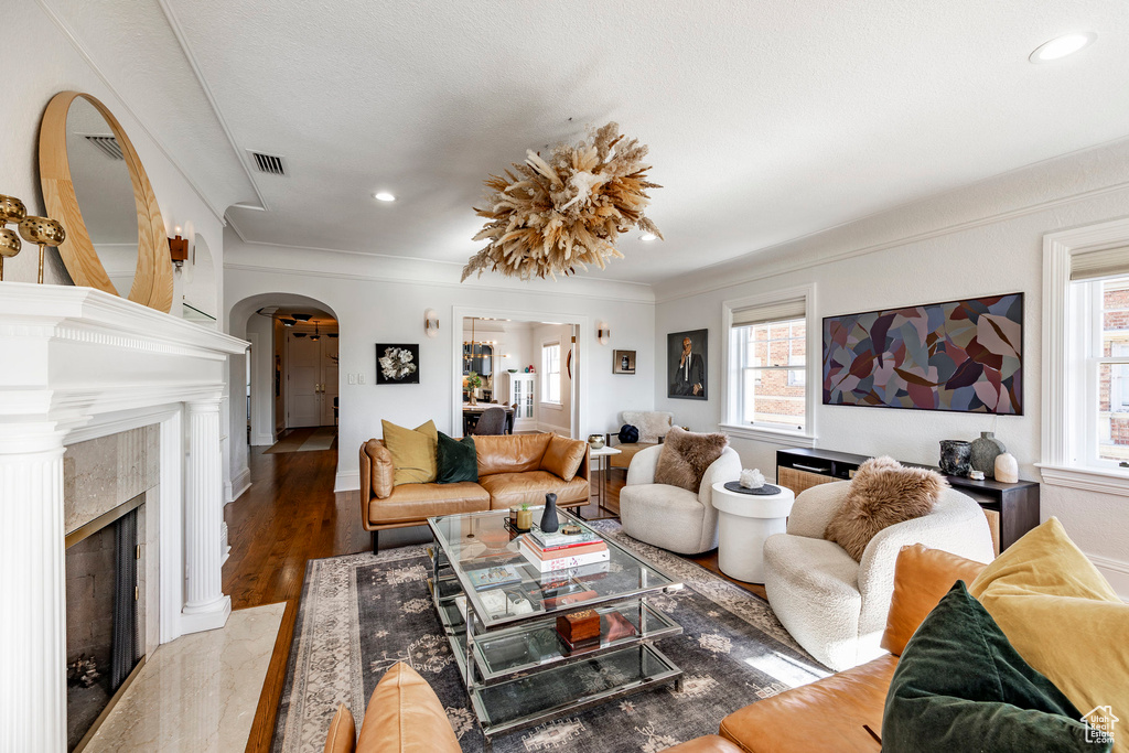 Living room with a high end fireplace, plenty of natural light, crown molding, and wood-type flooring