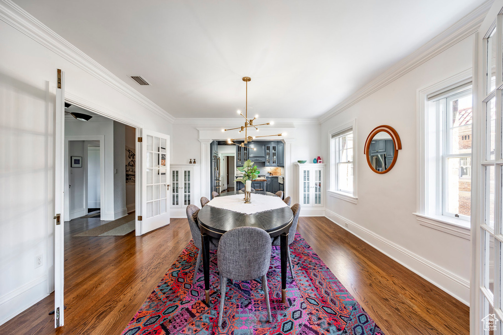 Dining space featuring french doors, dark wood-type flooring, crown molding, and an inviting chandelier