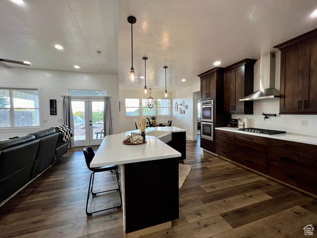 Kitchen with sink, a kitchen bar, wall chimney exhaust hood, dark wood-type flooring, and a kitchen island with sink