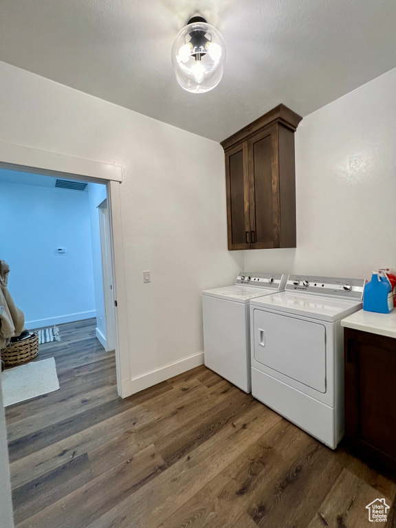 Clothes washing area with washer and clothes dryer, cabinets, and dark hardwood / wood-style flooring