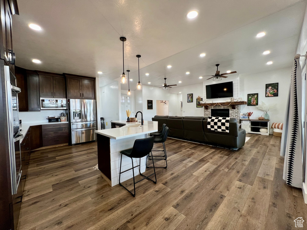 Kitchen with dark hardwood / wood-style flooring, a kitchen breakfast bar, a kitchen island with sink, dark brown cabinetry, and stainless steel appliances