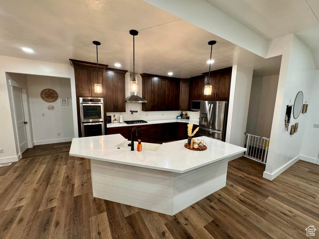 Kitchen with a kitchen island with sink, appliances with stainless steel finishes, sink, and dark hardwood / wood-style flooring