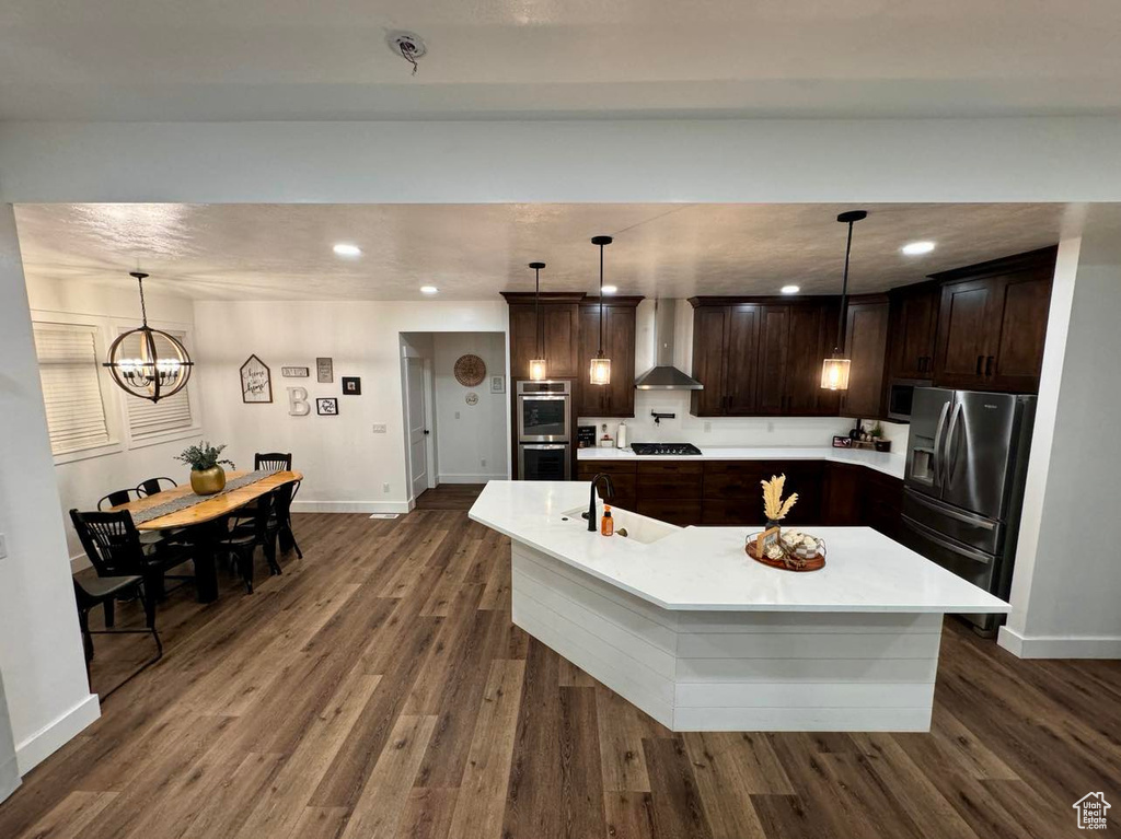 Kitchen with dark hardwood / wood-style flooring, hanging light fixtures, sink, wall chimney range hood, and appliances with stainless steel finishes