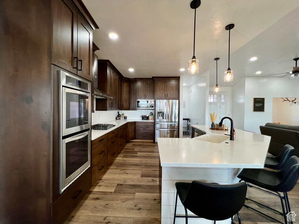 Kitchen with hanging light fixtures, appliances with stainless steel finishes, a kitchen breakfast bar, light wood-type flooring, and sink