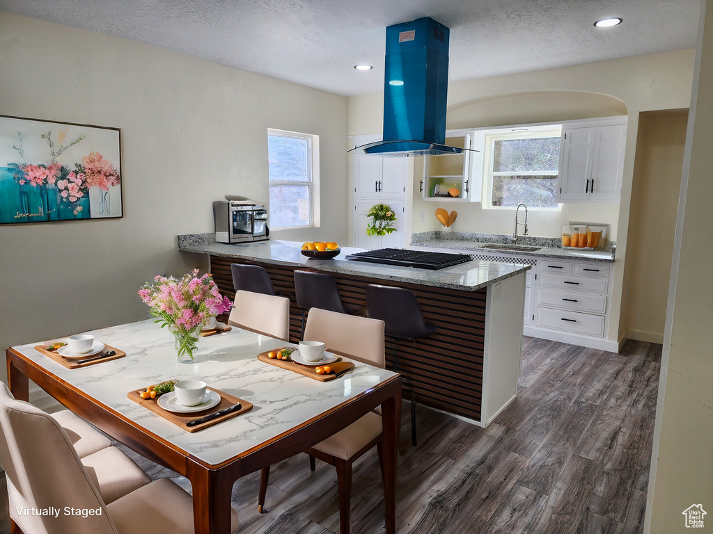 Kitchen featuring dark hardwood / wood-style flooring, island range hood, sink, light stone countertops, and white cabinetry