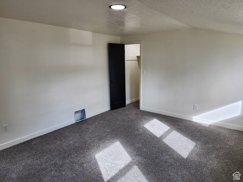 Empty room with dark colored carpet, a textured ceiling, and vaulted ceiling