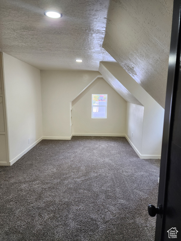 Bonus room with a textured ceiling, vaulted ceiling, and dark carpet