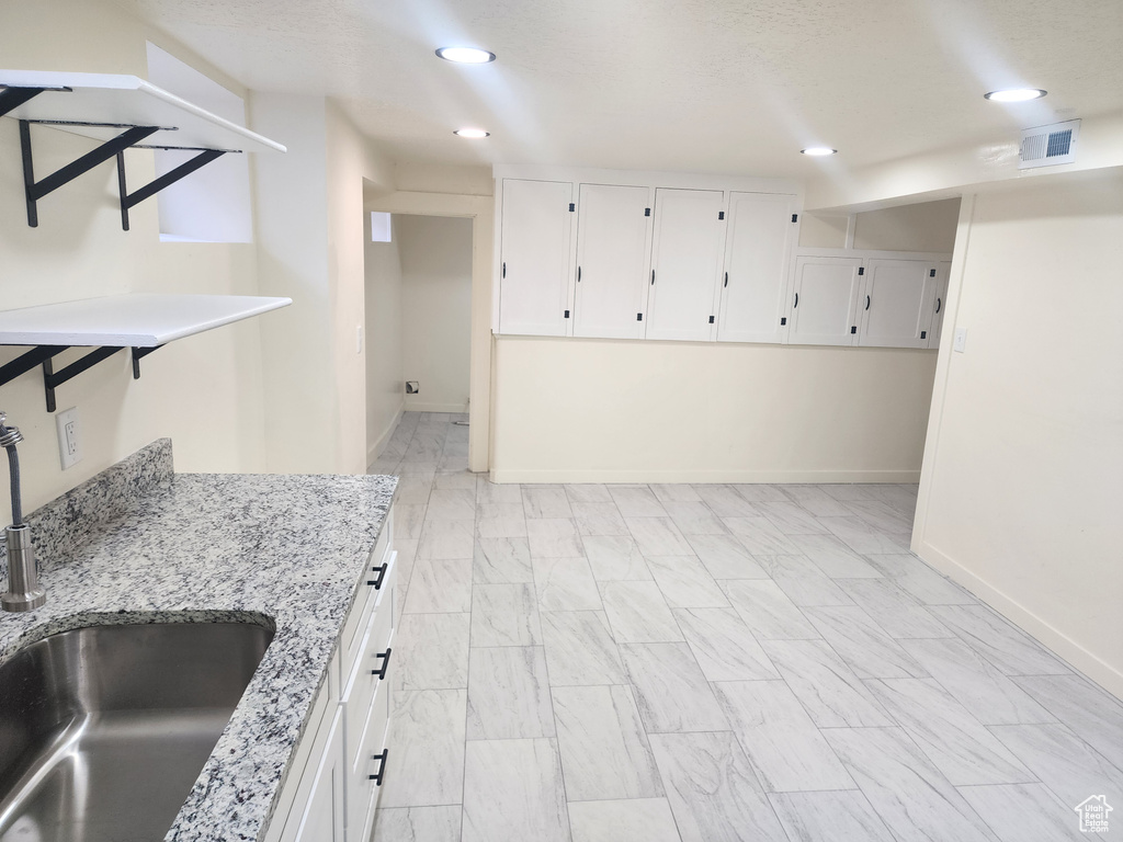 Kitchen featuring white cabinets, sink, and light stone counters