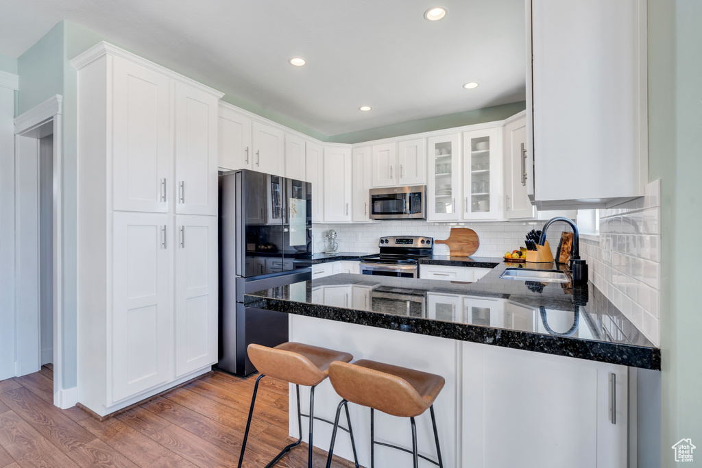 Kitchen with hardwood / wood-style flooring, appliances with stainless steel finishes, sink, and white cabinets