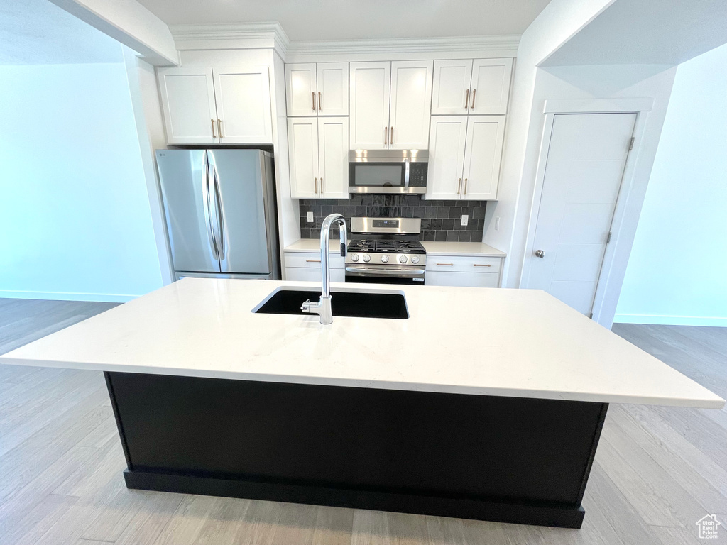 Kitchen with appliances with stainless steel finishes, backsplash, a center island with sink, white cabinetry, and light countertops