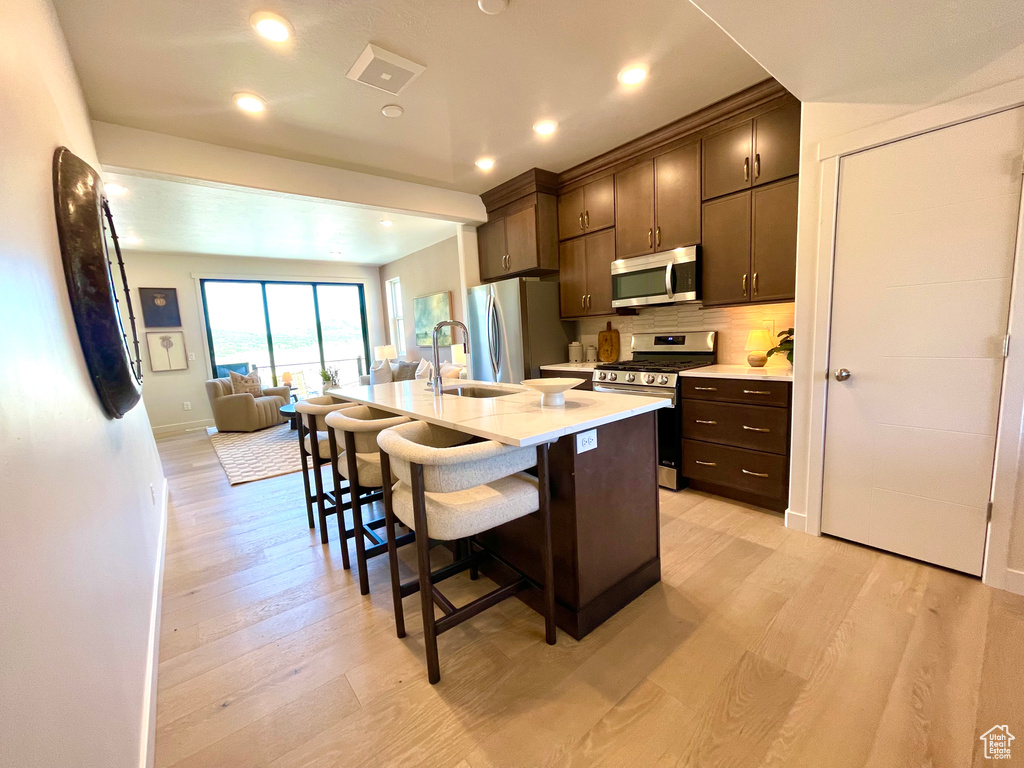 Kitchen with appliances with stainless steel finishes, a kitchen breakfast bar, dark brown cabinetry, light countertops, and light wood-type flooring