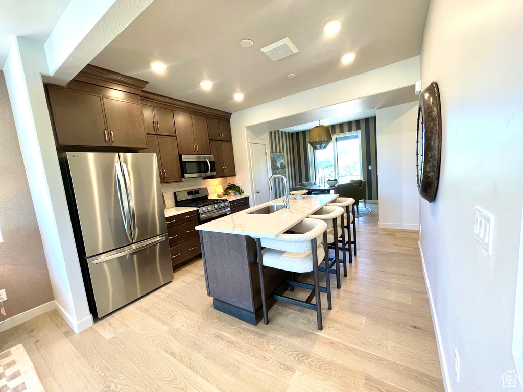Kitchen with stainless steel appliances, dark brown cabinetry, light wood-type flooring, a breakfast bar area, and an island with sink