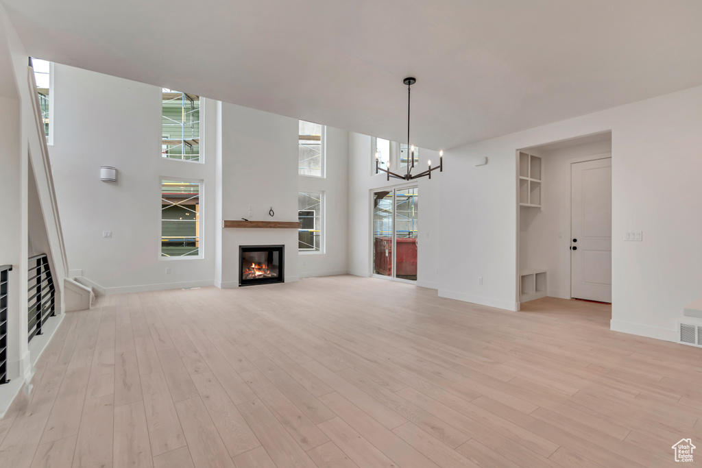 Unfurnished living room featuring a chandelier, baseboards, a glass covered fireplace, and light wood finished floors