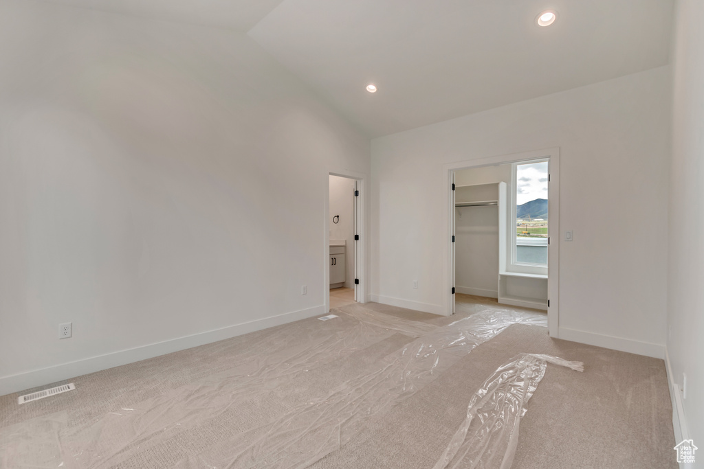 Unfurnished bedroom with a walk in closet, visible vents, light colored carpet, and lofted ceiling