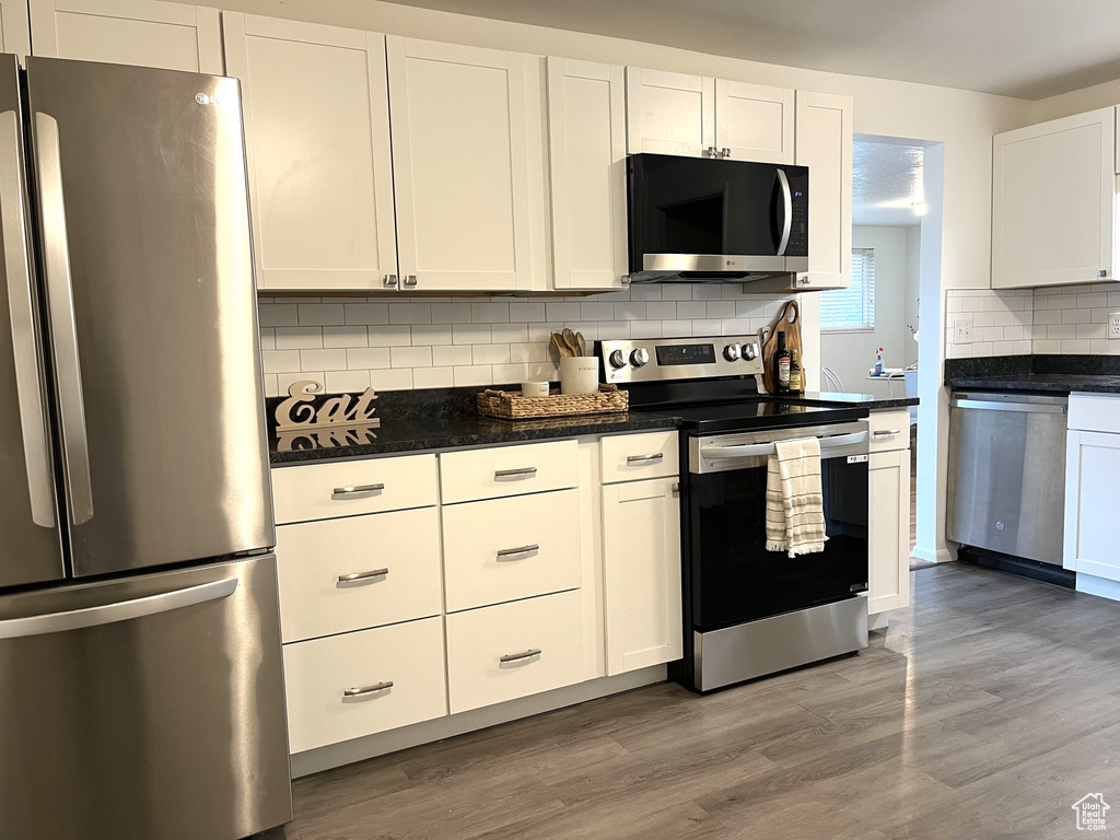 Kitchen featuring white cabinets, light wood-style floors, appliances with stainless steel finishes, and tasteful backsplash