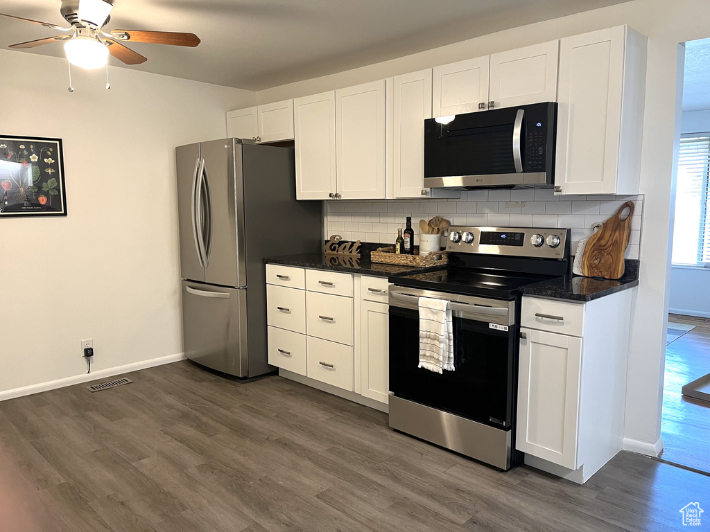 Kitchen featuring dark wood-style flooring, white cabinets, visible vents, tasteful backsplash, and appliances with stainless steel finishes