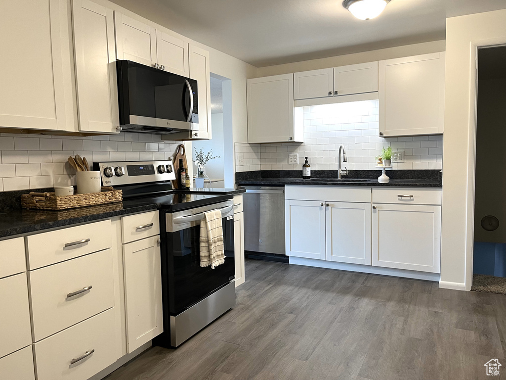 Kitchen with a sink, white cabinetry, appliances with stainless steel finishes, decorative backsplash, and dark wood-style flooring