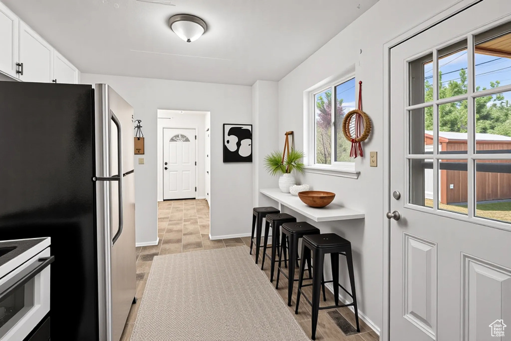 Kitchen featuring freestanding refrigerator, white cabinetry, range, and a breakfast bar