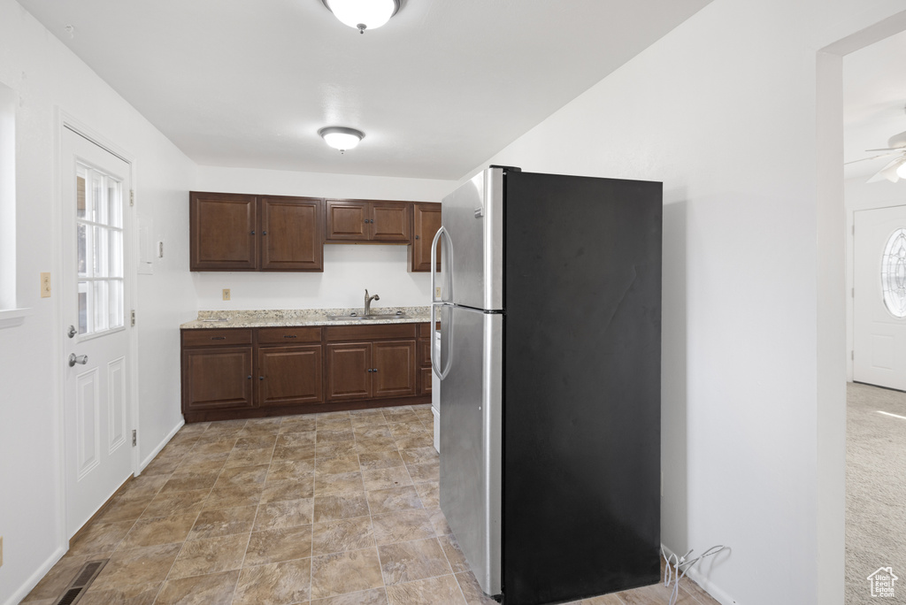Kitchen featuring a ceiling fan, a sink, freestanding refrigerator, light stone countertops, and dark brown cabinetry
