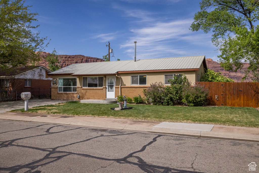 Ranch-style house featuring metal roof, fence, brick siding, a front yard, and stucco siding