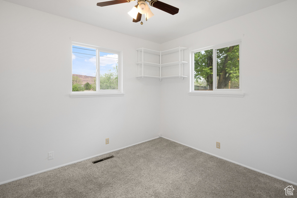 Empty room with carpet floors, visible vents, baseboards, and ceiling fan
