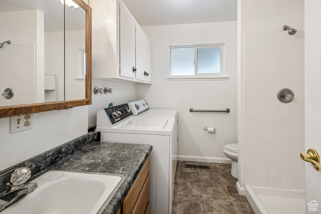 Bathroom with a tile shower, washing machine and dryer, baseboards, toilet, and vanity