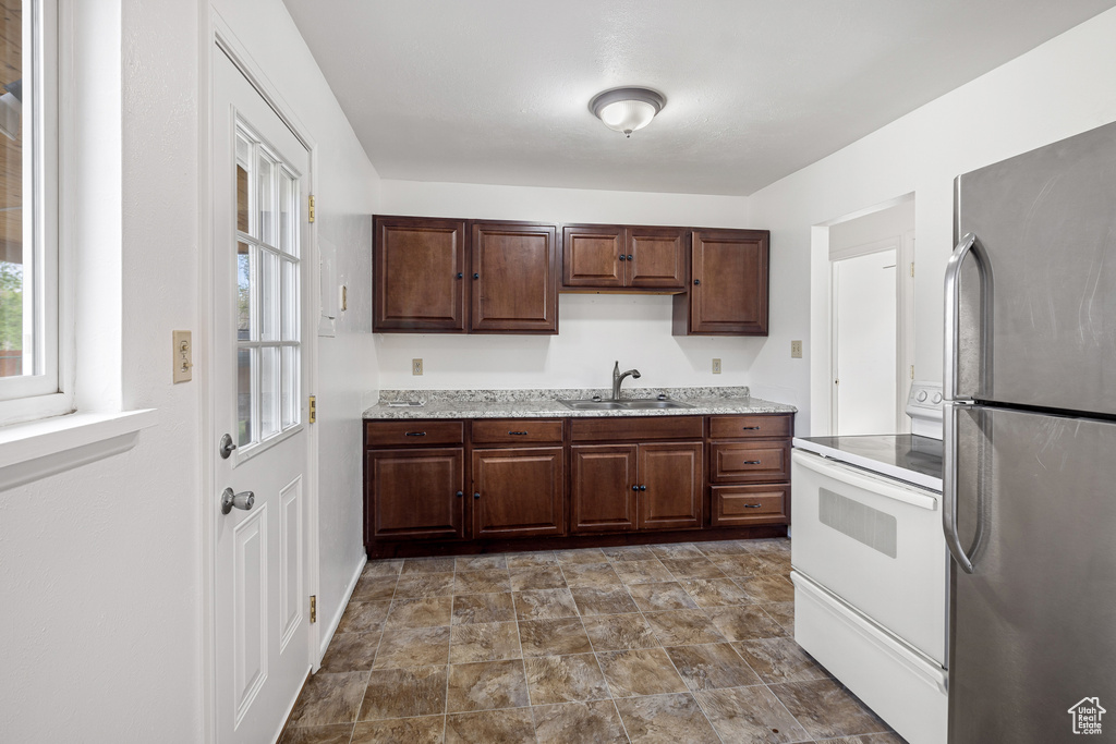 Kitchen featuring white range with electric cooktop, light stone countertops, freestanding refrigerator, and a sink