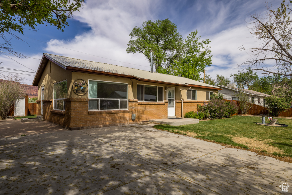 Ranch-style home with a front lawn, fence, metal roof, stucco siding, and brick siding