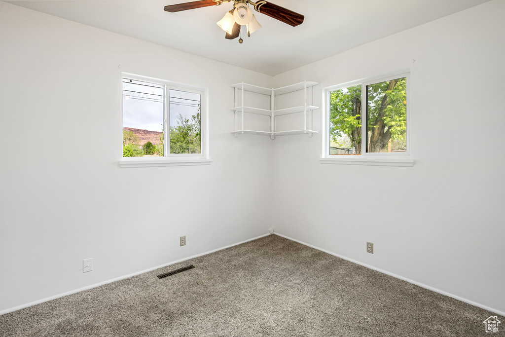 Carpeted empty room featuring a ceiling fan, visible vents, and baseboards