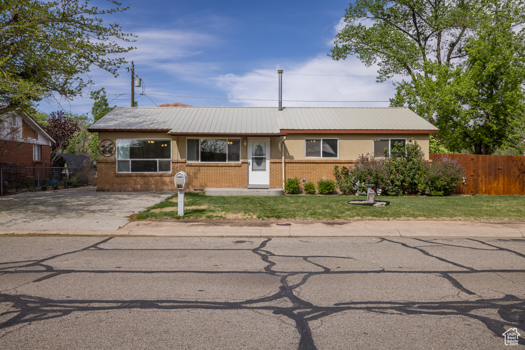 View of front facade with brick siding, fence, metal roof, and a front yard
