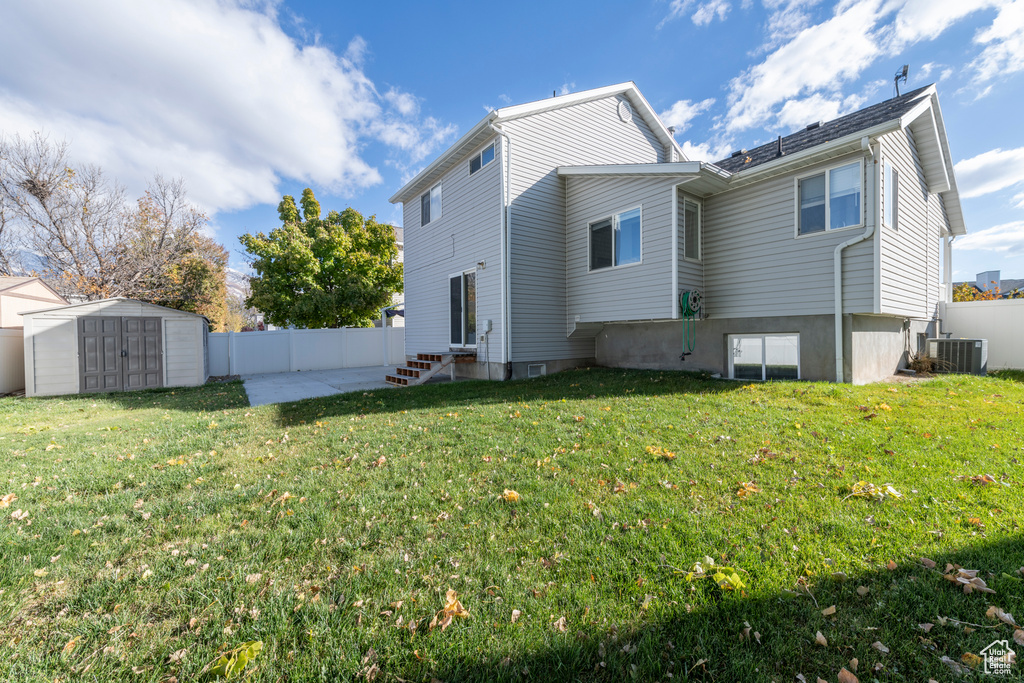 Back of house featuring a storage unit, a lawn, cooling unit, and a patio area