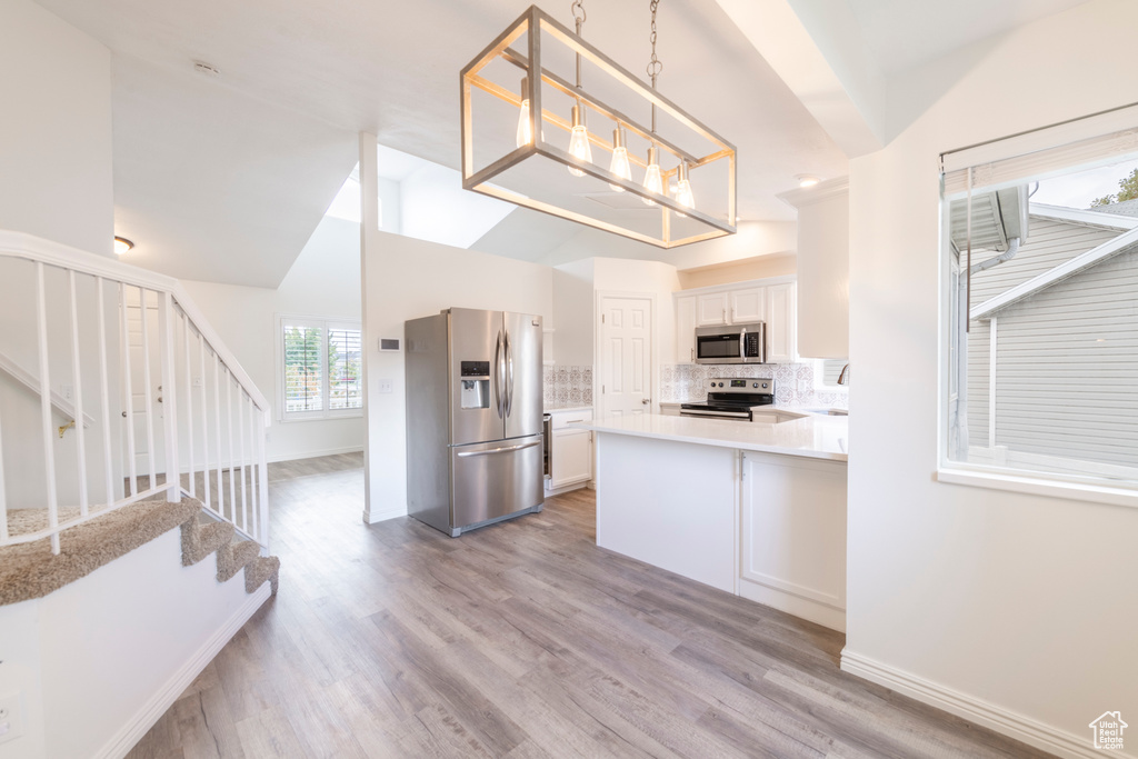 Kitchen featuring stainless steel appliances, tasteful backsplash, decorative light fixtures, light hardwood / wood-style flooring, and white cabinets