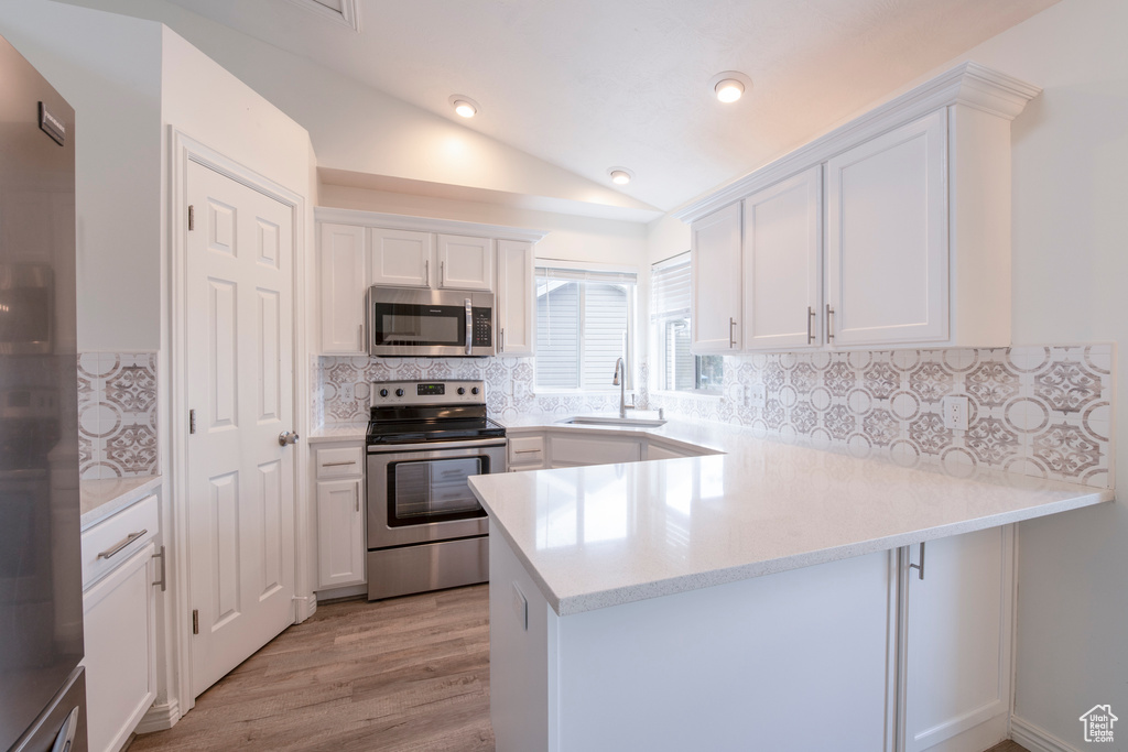 Kitchen featuring white cabinetry, kitchen peninsula, appliances with stainless steel finishes, and vaulted ceiling