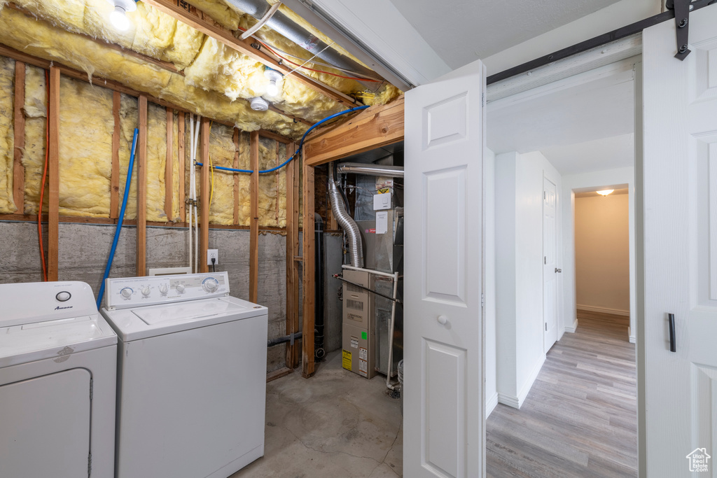 Washroom featuring heating unit, a barn door, light wood-type flooring, and washing machine and clothes dryer