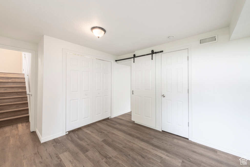 Unfurnished bedroom featuring dark wood-type flooring and a barn door