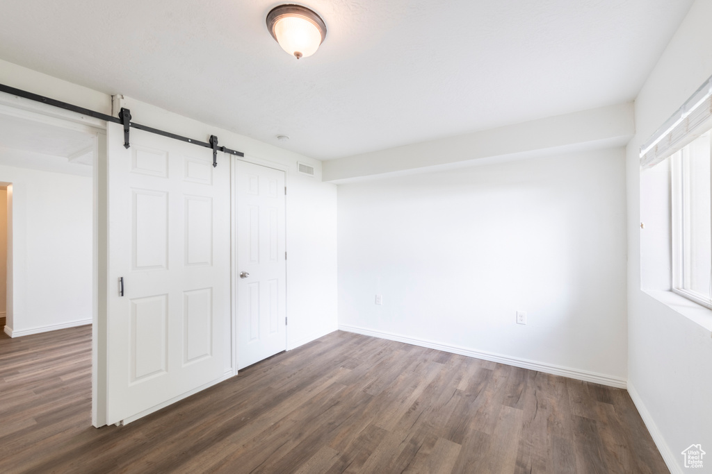 Unfurnished bedroom featuring a barn door, a closet, and dark wood-type flooring