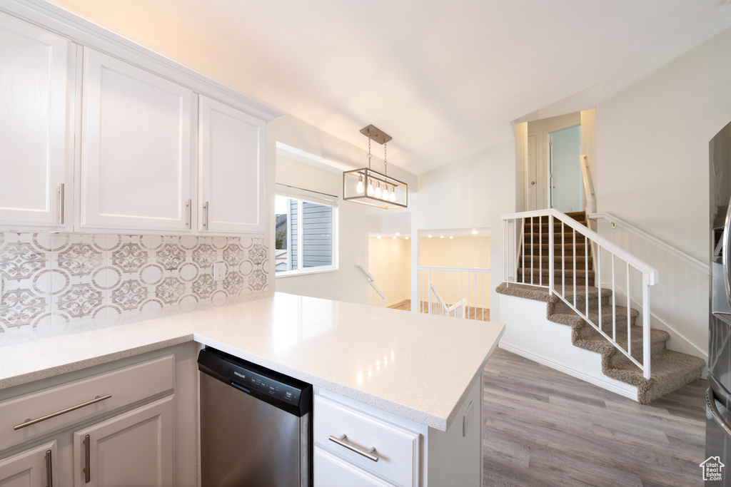 Kitchen with stainless steel dishwasher, wood-type flooring, white cabinetry, and tasteful backsplash