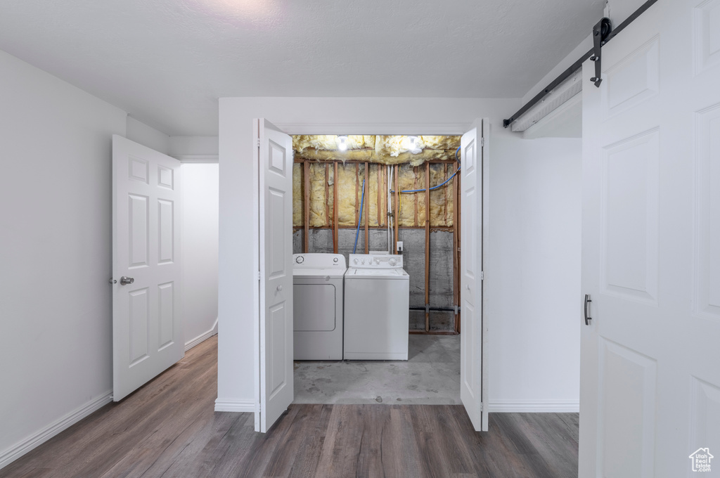 Laundry area with washing machine and dryer, a barn door, and wood-type flooring