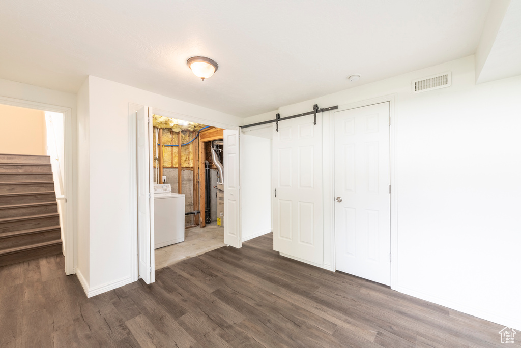 Unfurnished bedroom featuring ensuite bath, dark hardwood / wood-style floors, washer / dryer, a barn door, and a closet