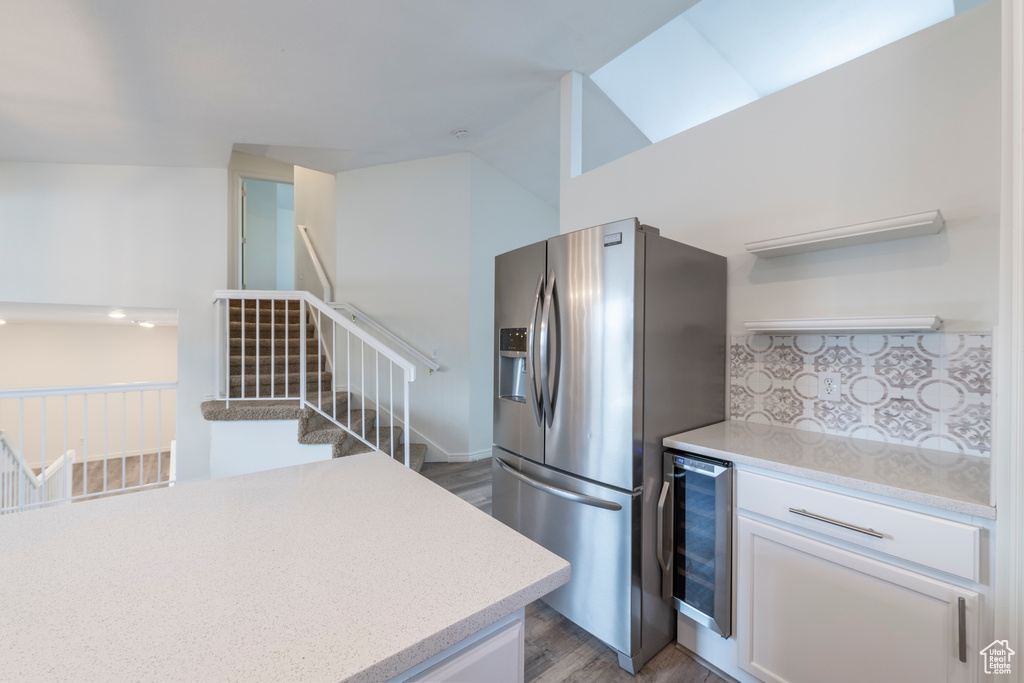 Kitchen featuring white cabinetry, beverage cooler, stainless steel fridge, light wood-type flooring, and vaulted ceiling