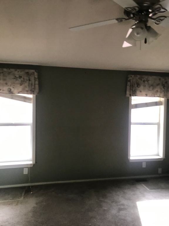 Empty room with ceiling fan, dark carpet, and plenty of natural light