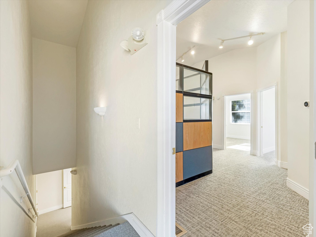 Hallway with light colored carpet, rail lighting, and high vaulted ceiling