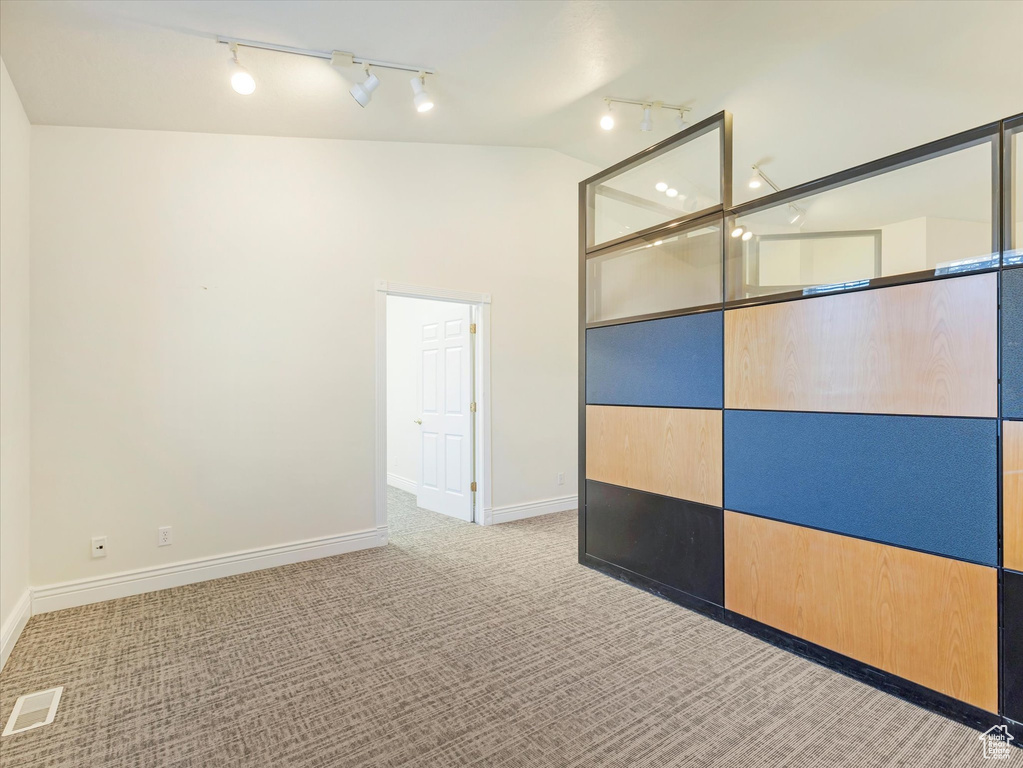 Interior space with rail lighting, light carpet, and vaulted ceiling