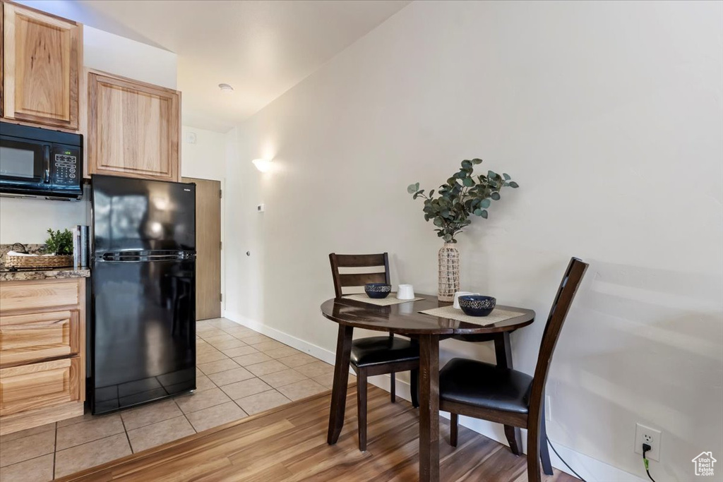 Kitchen with light wood-type flooring, light brown cabinetry, black appliances, and lofted ceiling