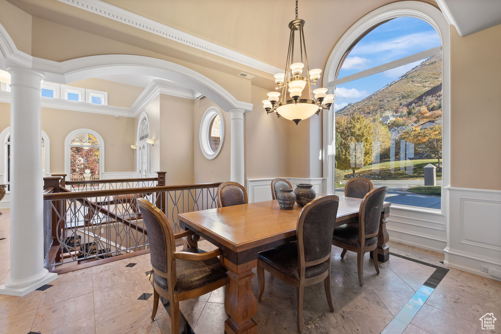 Dining area with a mountain view, ornamental molding, a notable chandelier, a high ceiling, and decorative columns