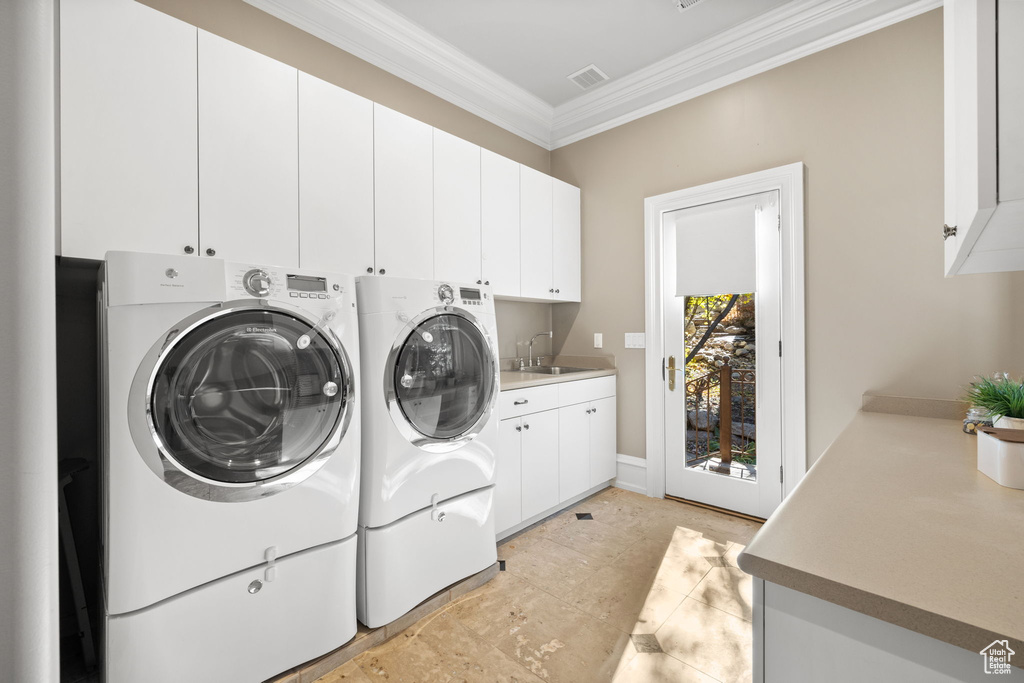 Clothes washing area with cabinets, sink, washer and clothes dryer, and ornamental molding